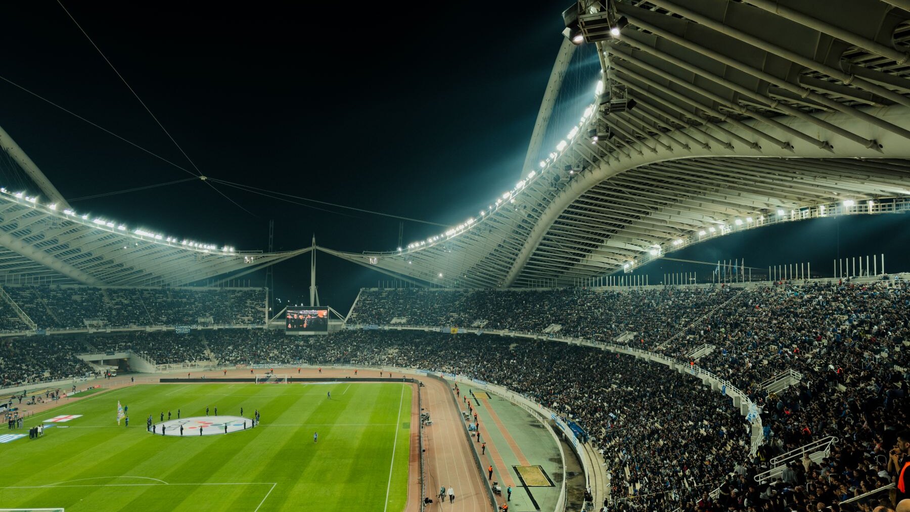 Soccer supporters filling a stadium under floodlights at night