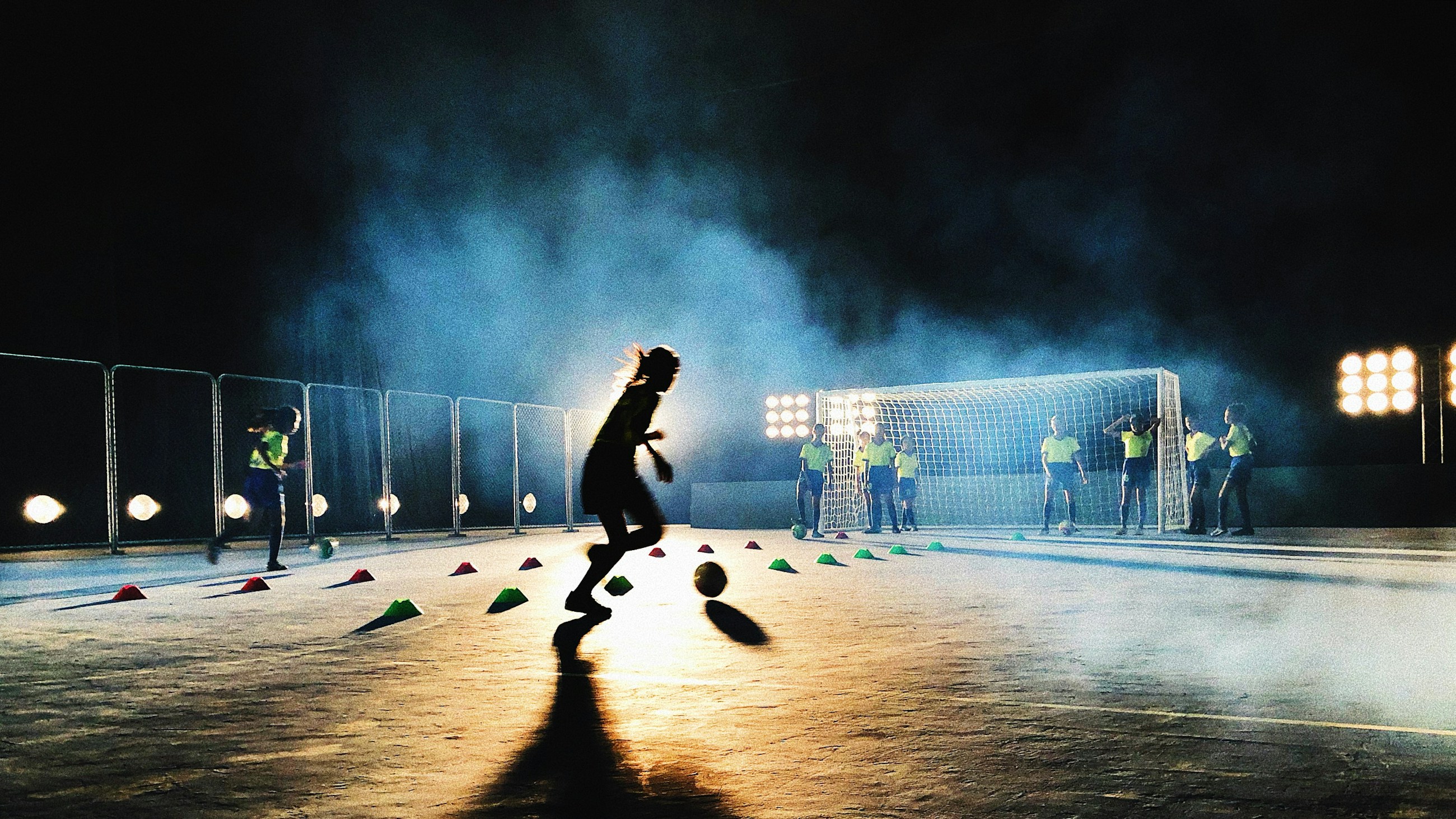 A player dribbling a soccer ball through a floodlit training session at night